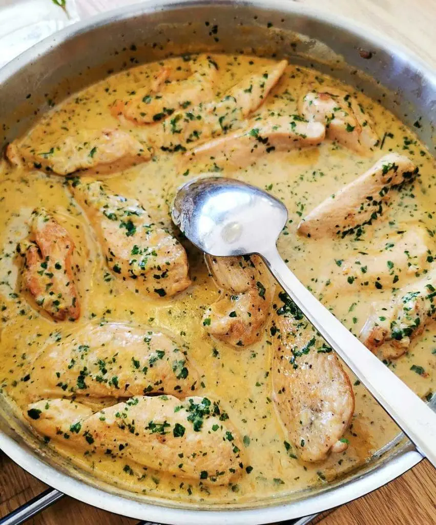 Kyckling i currysås 7 Kycklingdelar i en gräddig persiljesås i en stekpanna med en sked.