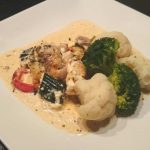Gratinerad torsk serverad med broccoli och blomkål på en vit tallrik.