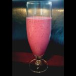 Smoothie med jordgubbar och blåbär i ett högt glas på en mörk yta.