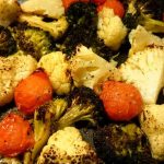 Rostade bitar av blomkål och broccoli tillsammans med körsbärstomater i en stekpanna.