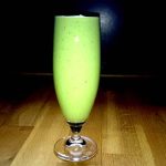 Grön smoothie i ett högt glas med en slät yta och skum på toppen.