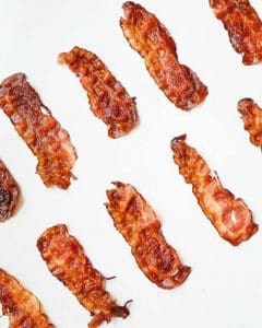 Flera skivor av stekt bacon placerade på en vit bakgrund.