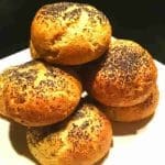 En hög av hembakade bröd med vallmofrön på toppen, placerade på en vit tallrik.