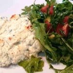 En portion fetaost och purjobakad torsk serverad med en grönsallad bestående av ruccola och tomater.