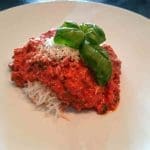 En tallrik med köttfärssås toppad med basilika och riven parmesanost.