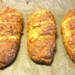 Tre zuchinibaguetter med sesamfrön på en bakplåt av bakpapper.