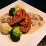 Köttfärslimpa skivad och serverad med sås, broccoli och blomkål på en vit tallrik.