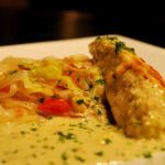 Pestogratinerad kycklingfilé serverad med grönsaksblandning på en vit tallrik.