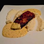 En portion skinkschnitzel med sås och puré på en vit tallrik.