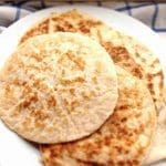 Tre glutenfria naanbröd på en vit tallrik med en rutig duk i bakgrunden.