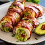 Guacamolefylld kycklingfilé inlindad i bacon på en tallrik med avokado.