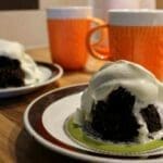 Mugcake serverad med vispgrädde på en tallrik, med två orange muggar i bakgrunden.