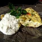 Grönsaksomelett serverad med en vit sås och örter på en glasfat.