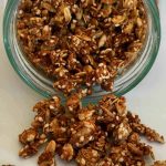 En glasburk med granola som har en blandning av nötter och frön, delvis utspilld på en yta.