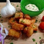 Friterad halloumi serverad med vitlök, tomater och en grön skål med sås.