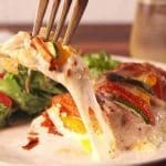 En portion kyckling med grönsaker och smält ost på en tallrik med en sallad vid sidan.
