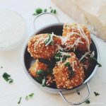 Friterade bollar täckta med sesamfrön, parmesan och färska örter i en metallskål.