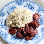 En tallrik med skivad korv och potatismos dekorerad med dill på en blå och vit mönstrad tallrik.