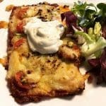 En bit pizza med smält ost, tomater och en klick gräddfil på en tallrik.