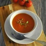En skål med tomatsoppa på en träskärbräda med tre färska tomater i bakgrunden.