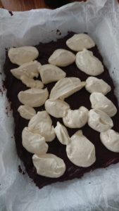 En chokladkaka med klumpar av gräddfyllning på toppen, placerad på ett bakplåtspapper.