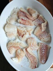 En skål med råa fiskfiléer som är skurna i bitar och kryddade med svartpeppar.