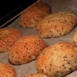 Färska kesobröd med frön bakade på en plåt med bakpapper.
