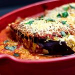 Auberginegratäng med tomatsås och ost, gräddad i en röd ugnsform.
