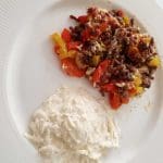 En tallrik med köttfärsrätt bestående av köttfärs, paprika och tomater, serverad med en vit sås.