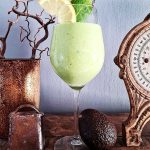 Grönt smoothie i ett glas med avokado och spenat, dekorerat med en citronskiva och mynta.