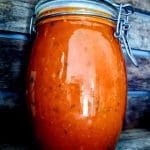 En glasburk med inlagd tomatsås som har en röd-orange färg och synliga örter.