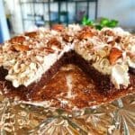 En kladdkaka med grädde och nötter, skuren i bitar och placerad på ett glasfat.