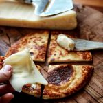 En hand som håller en bit LCHF-bröd med smör på en träskärbräda.