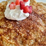 En gyllenbrun pannkaka toppad med vispgrädde och färska bär på en vit tallrik.