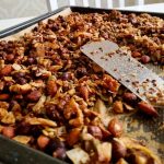 En plåt med granola som innehåller nötter och frön, delvis skrapad med en spatel.