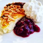 En skiva ostkaka med mandel, grädde och bärsås på en vit tallrik.