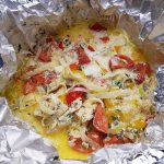 Foliegrillad abborre med grönsaker som tomater, lök och kryddor i aluminiumfolie.