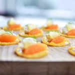 Ostchips toppade med löjrom, citron och dill på en träbricka.
