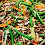 En blandning av haricots verts, köttfärs, morötter och kål i en stekpanna.