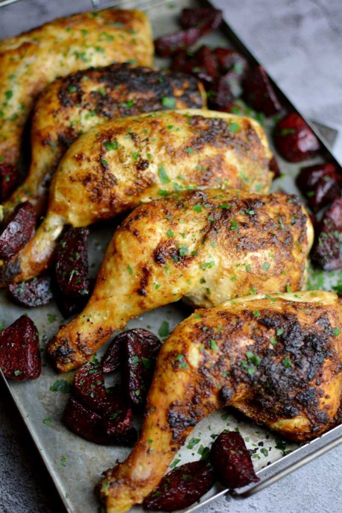 Grillade kycklingklubbor placerade på en plåt med rostade rödbetor runtom. Grillade kycklingklubbor placerade på en plåt med rostade rödbetor runtom.