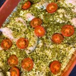 Ugnsform med kycklingfiléer täckta av pesto och skivade tomater.