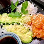 En tallrik med lax sashimi, avokado, gurka och sesamfrön, serverad med sojasås.