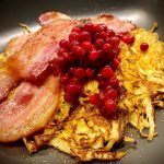 En tallrik med raggmunk toppad med bacon och lingon.