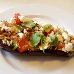 Ugnsbakad aubergine fylld med fetaost, tomater, valnötter och örter på en vit tallrik.