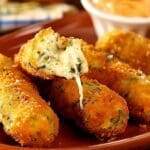 Friterade spenat- och mozzarellasticks på en tallrik med en dipp i bakgrunden.
