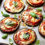 Aubergine skivor toppade med tomat, ost och basilika på en plåt.