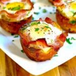 Muffins med bacon och ägg, garnerade med grönsaker på en vit tallrik.
