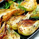Ugnsrostad lök skuren i halvor, placerad på en plåt med dill och kryddor.