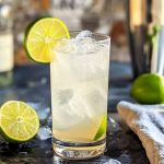 Gin Rickey cocktail med is och lime i ett glas, med limehalvor på sidan.