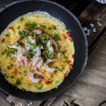 En räkomelett med örter och parmesan i en stekpanna på en träyta.